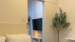 A hotel room with a bed, a bedside table, a lamp, a plant, and a bathroom visible through an open door. - Fully Furnished Makati Condo With Fast Wi-fi and Queen Bed (Makati)