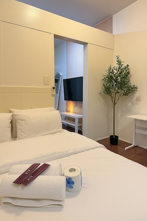 Ein Hotelzimmer mit Bett, Nachttisch, Lampe, Pflanze und einem durch eine offene Tür einsehbaren Badezimmer.