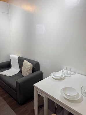 Ein Zimmer mit einer grauen Couch, einem weißen Tisch mit Tellern und Gläsern sowie einem weißen Kissen.