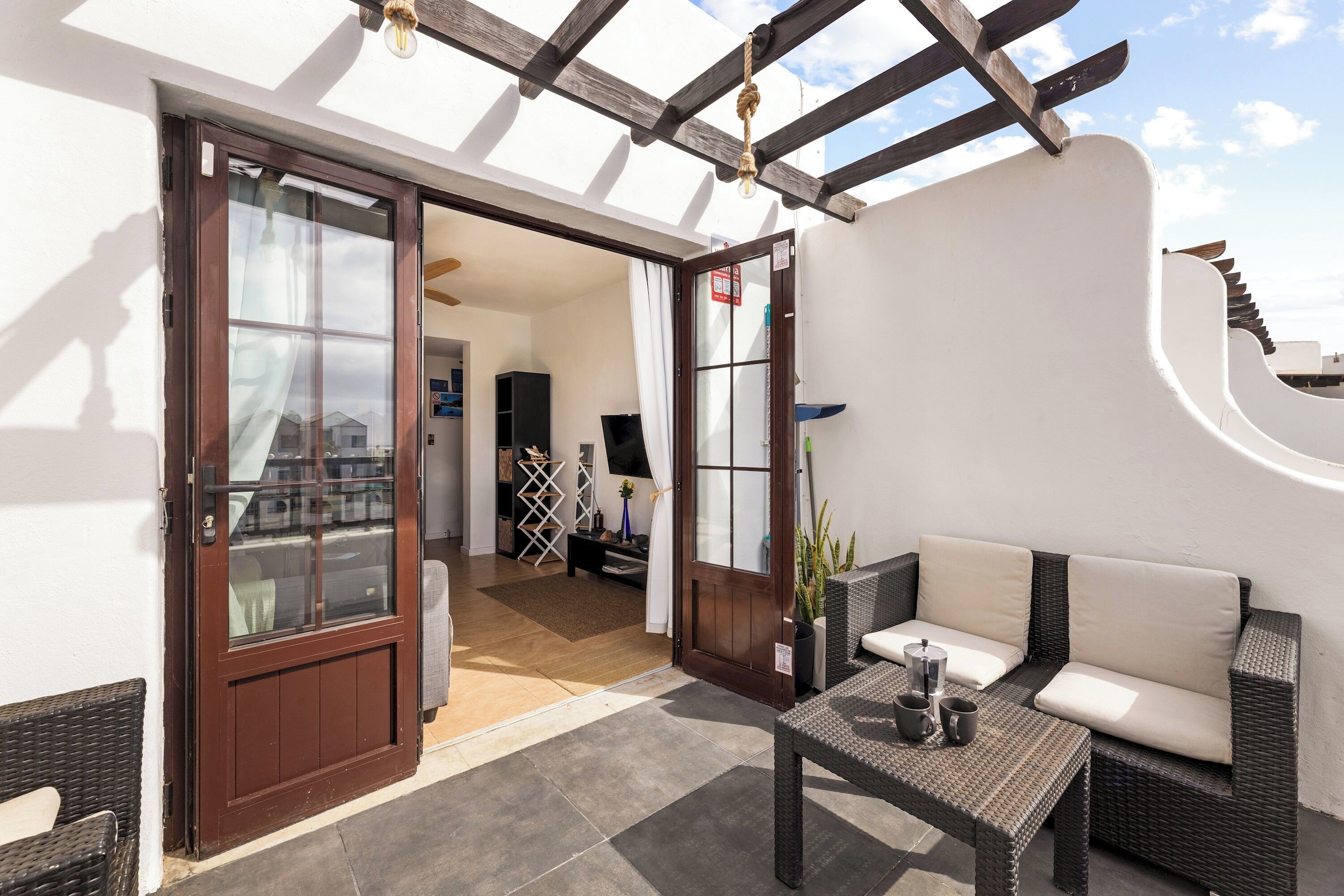 Eine Terrassenanlage mit einer Rattan-Couch, einem Tisch mit zwei Tassen und einer Holz-Pergola.