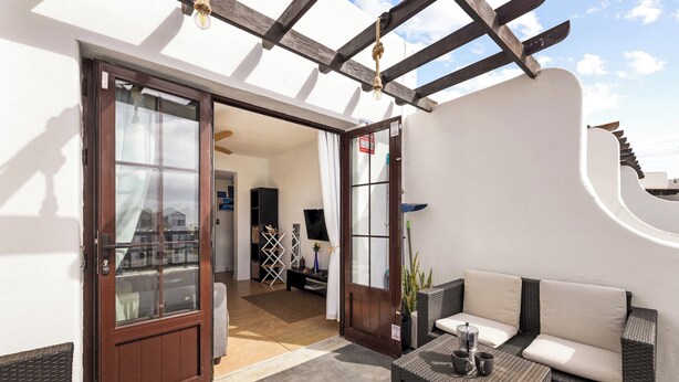 En terrasse med en fletsofa, et bord med to kopper, og en træpergola.