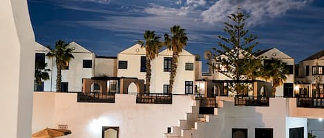 A nighttime view of a hotel with a swimming pool, palm trees, and a moon in the sky.