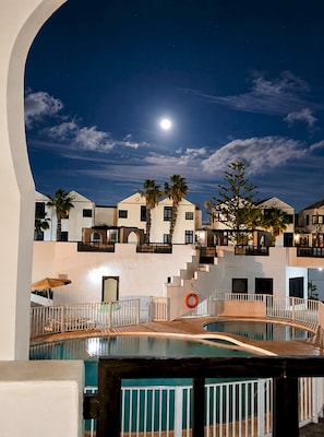 Ein Hotel bei Nacht mit Schwimmbad, Palmen und Mond am Himmel.