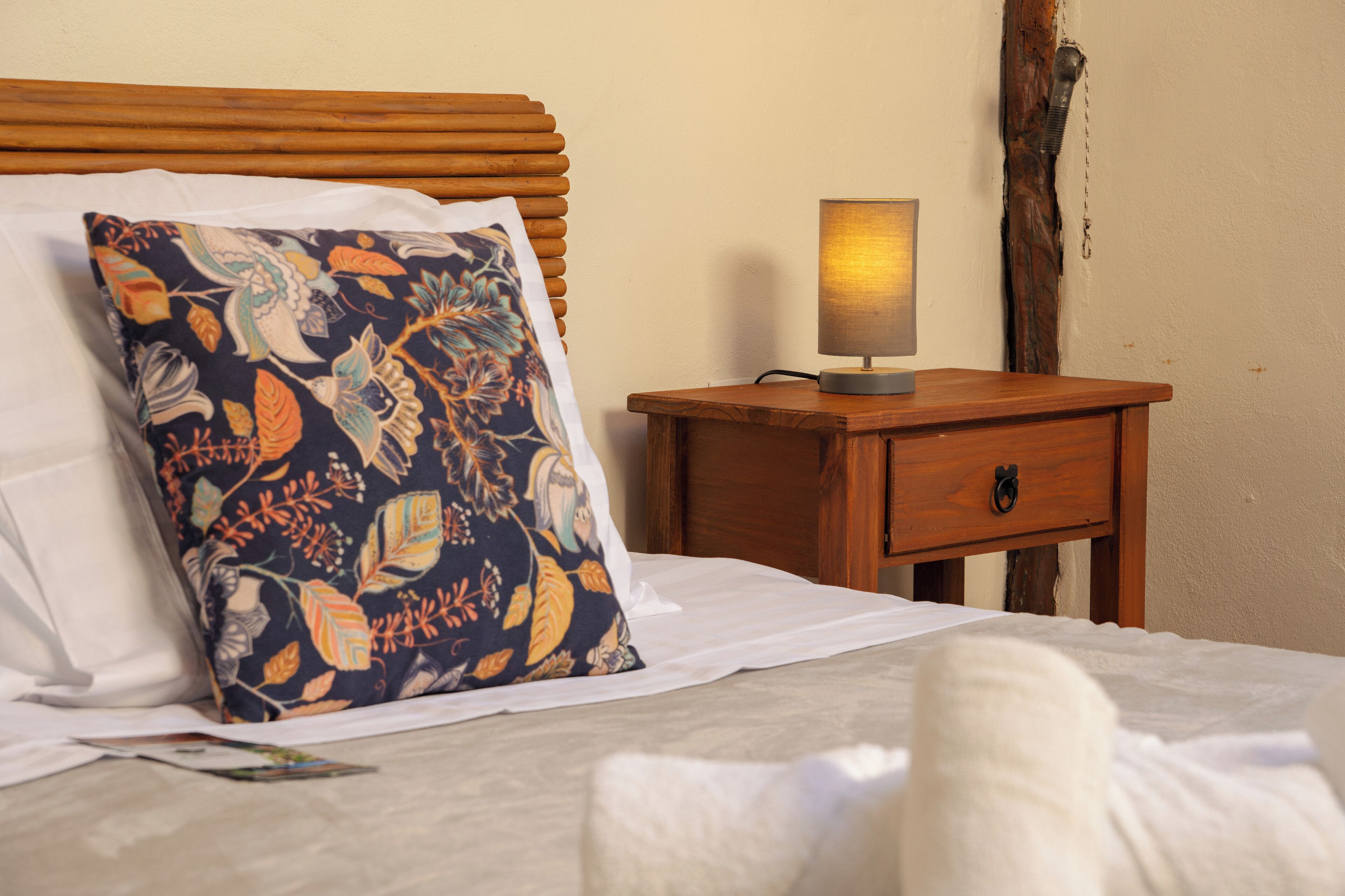 A neatly made bed with a floral pillow, a bedside table with a lamp, and a wooden nightstand.