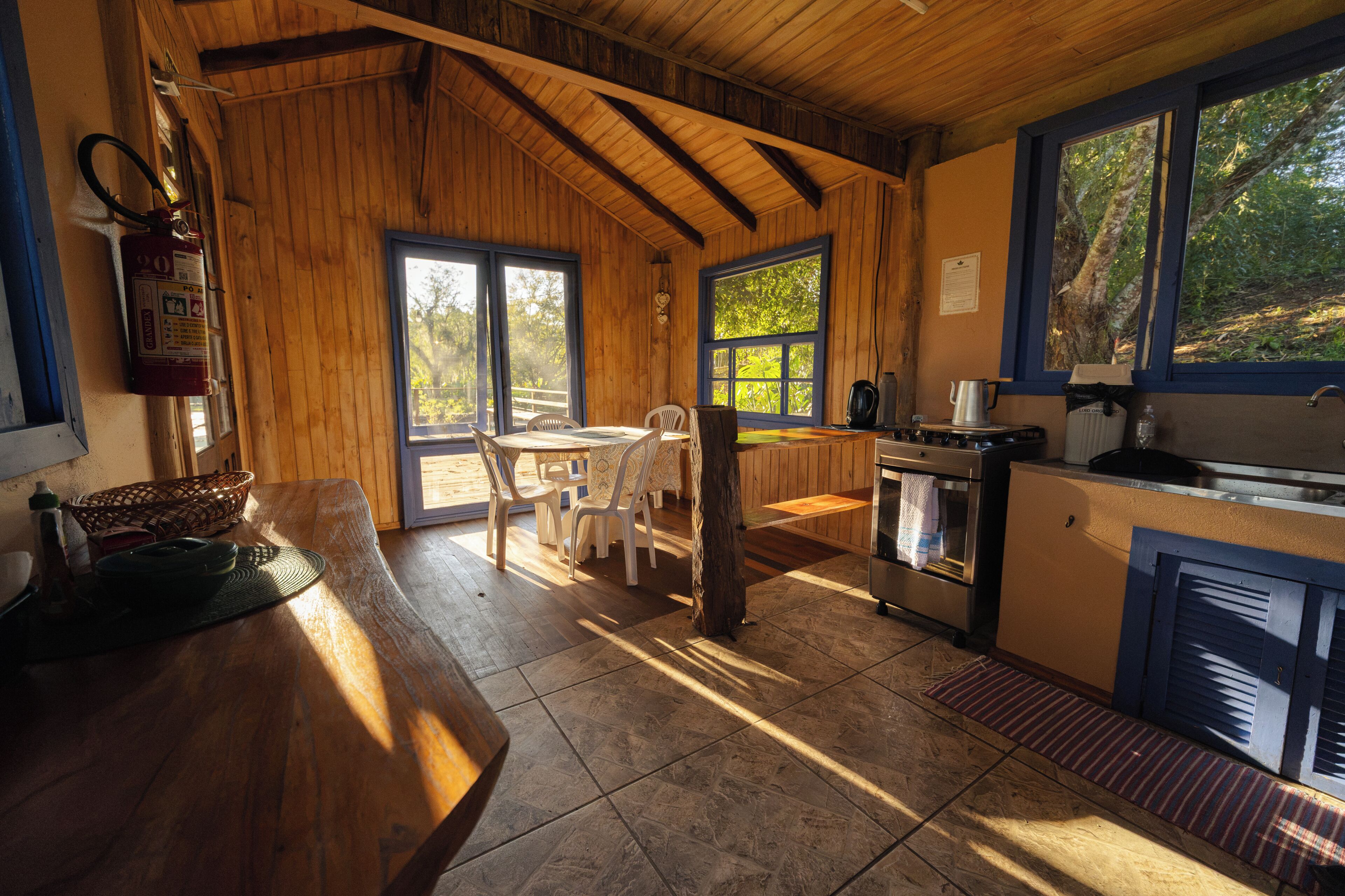 A wooden interior with a dining area, kitchen, and large windows.