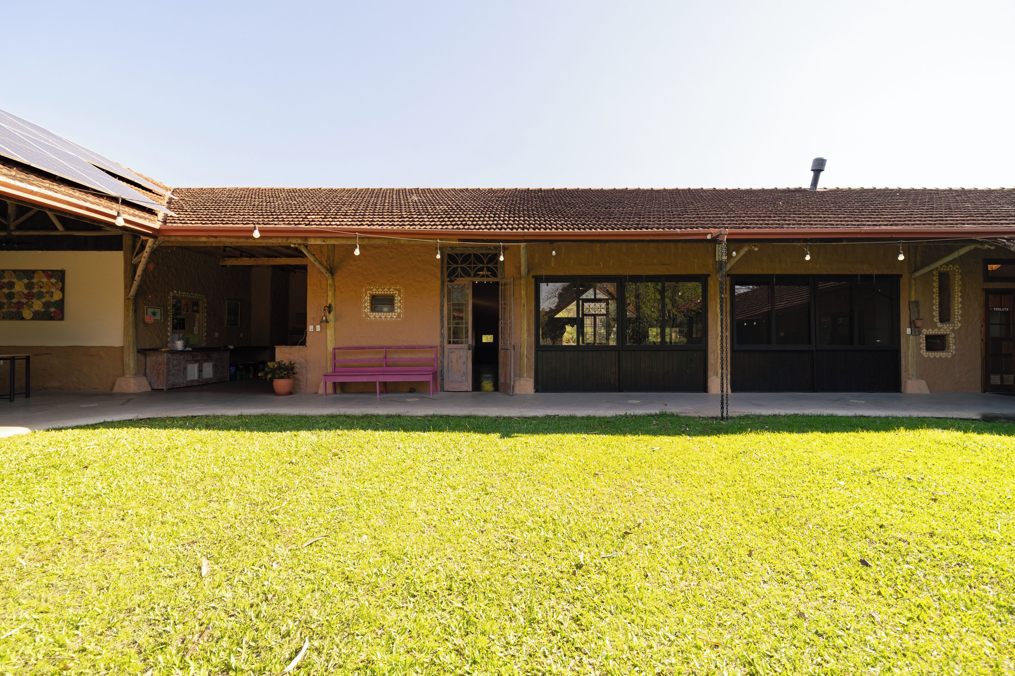 A building with a covered patio area, a bench, and a well-maintained lawn.
