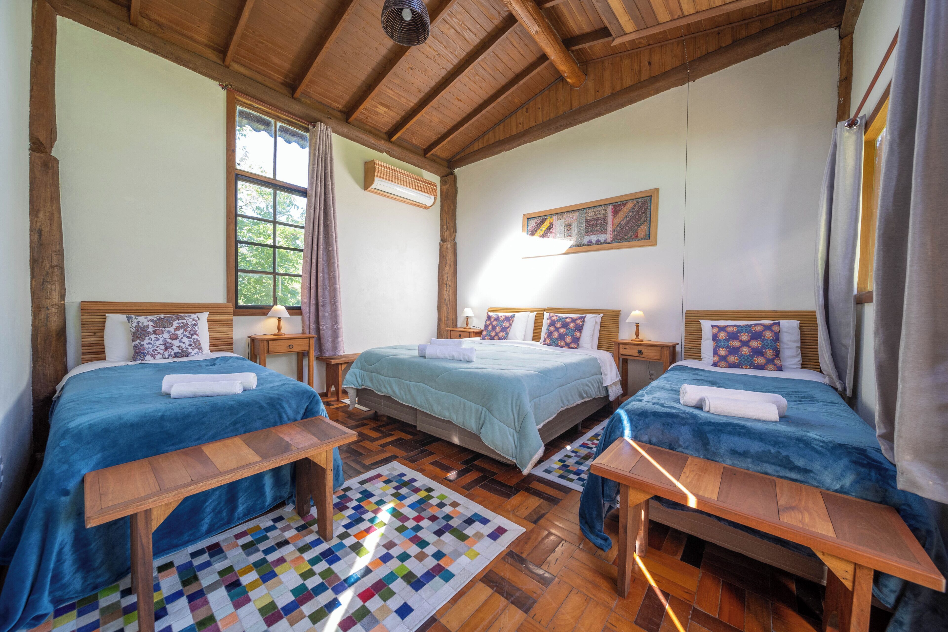 Quarto com duas camas, teto de madeira, janela e tapete colorido.