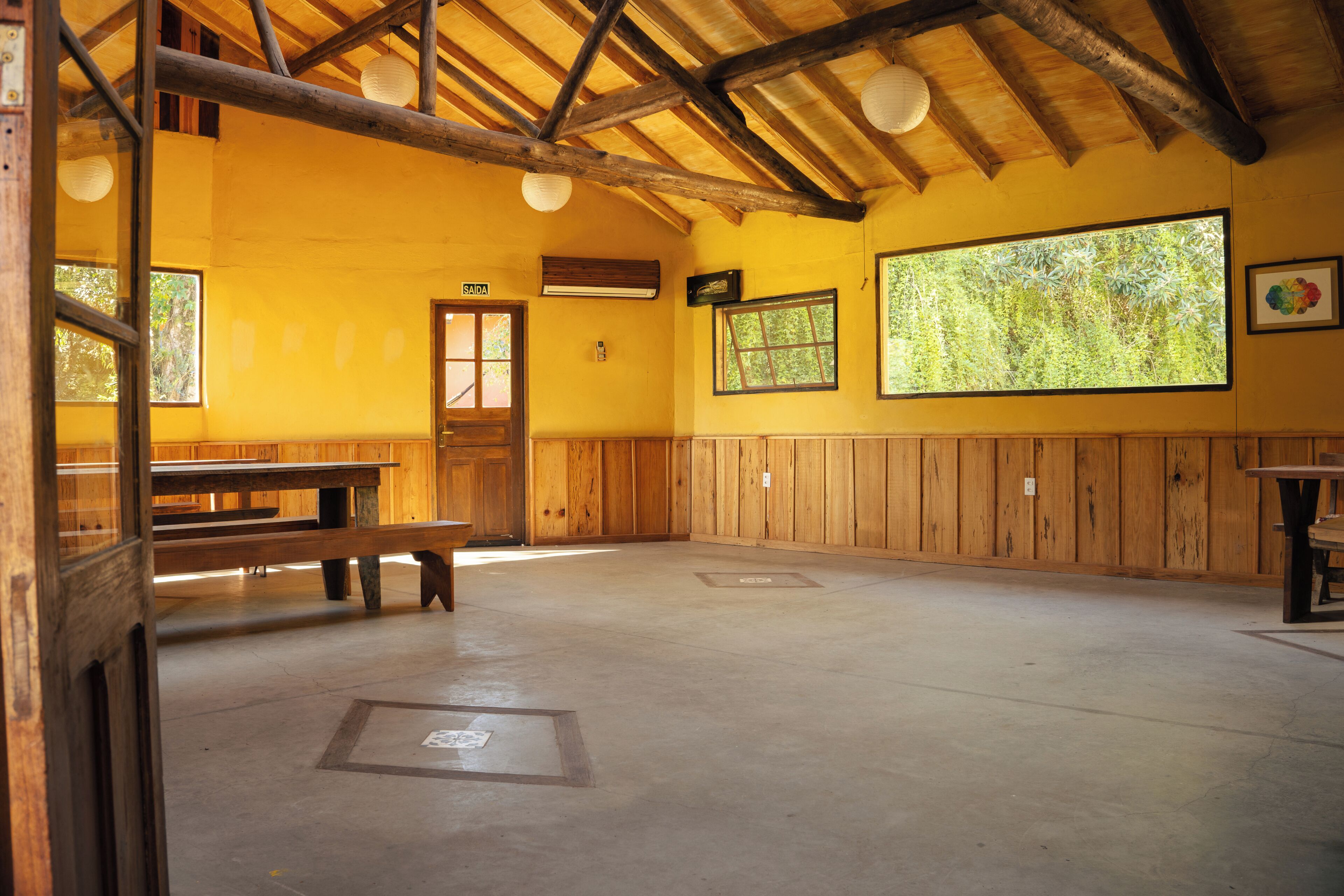 A room with wooden walls, a high ceiling with exposed beams, a wooden bench, and a door labeled 'SAIDA'.