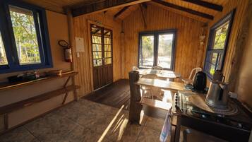A rustic kitchen with wooden walls, a tiled floor, a stove, and a window overlooking greenery.