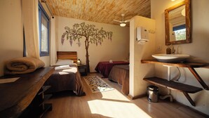 Un dormitorio con techo de madera, un adhesivo de árbol en la pared, una mesita de noche, una cama, un tocador y un baño con lavamanos y espejo.