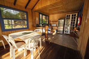 Cocina rústica con paredes de madera, una mesa de comedor con sillas, un refrigerador y una ventana con vistas a la vegetación.