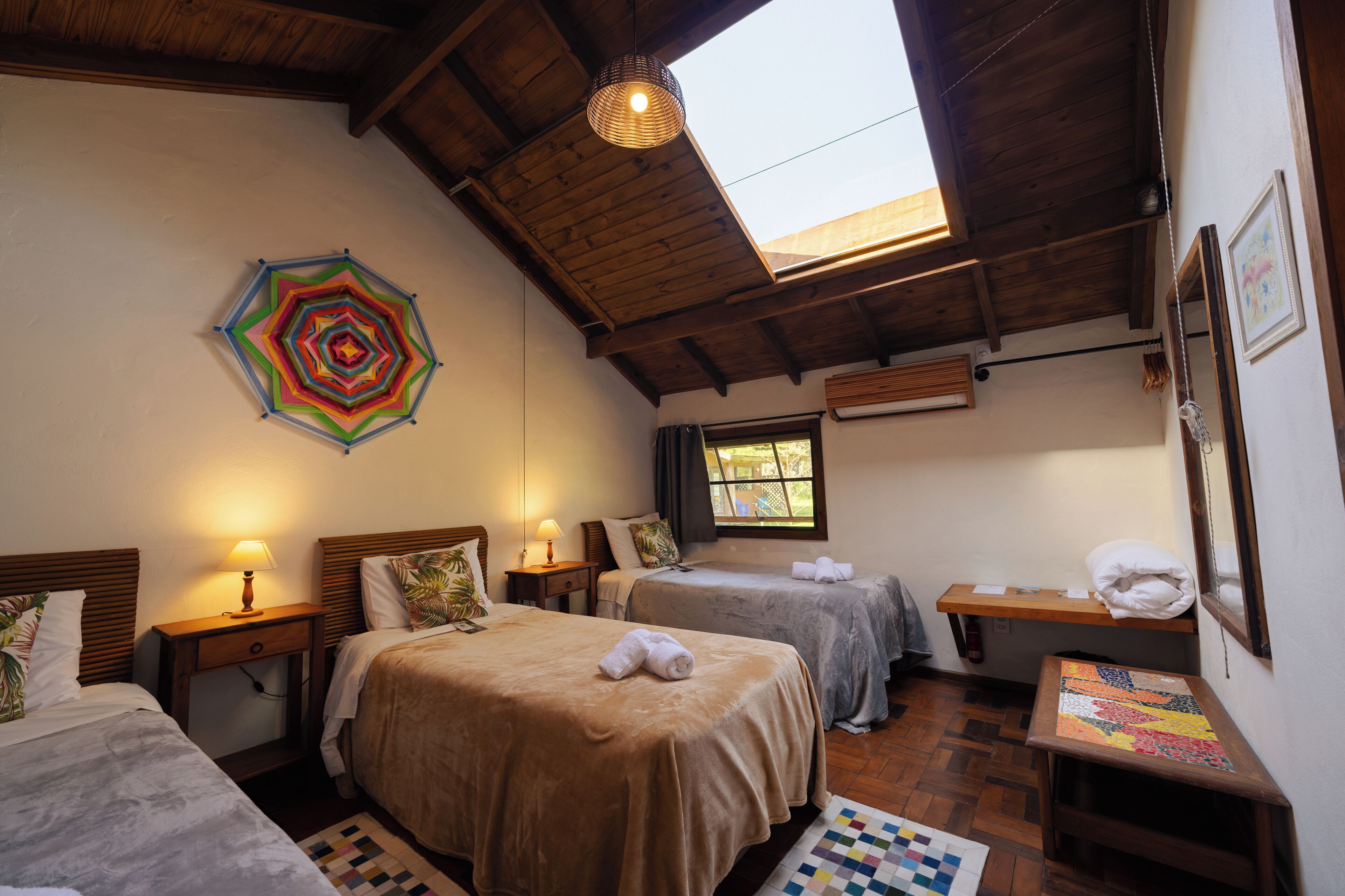 Una camera d'albergo con due letti, una ventola a soffitto, una finestra con tende e un'opera d'arte appesa al muro.