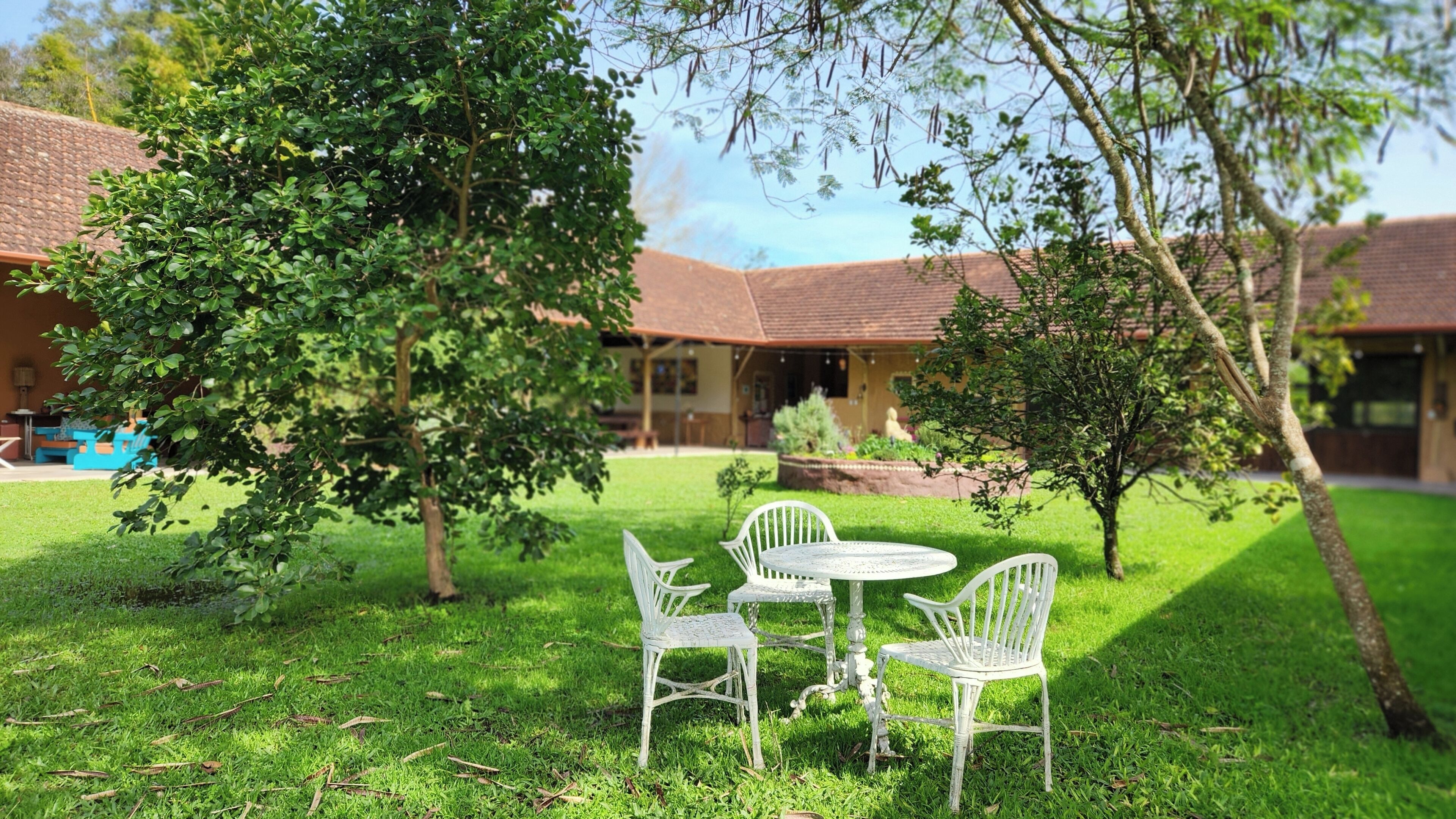 A courtyard with a table and chairs, surrounded by trees and a building with a tiled roof.