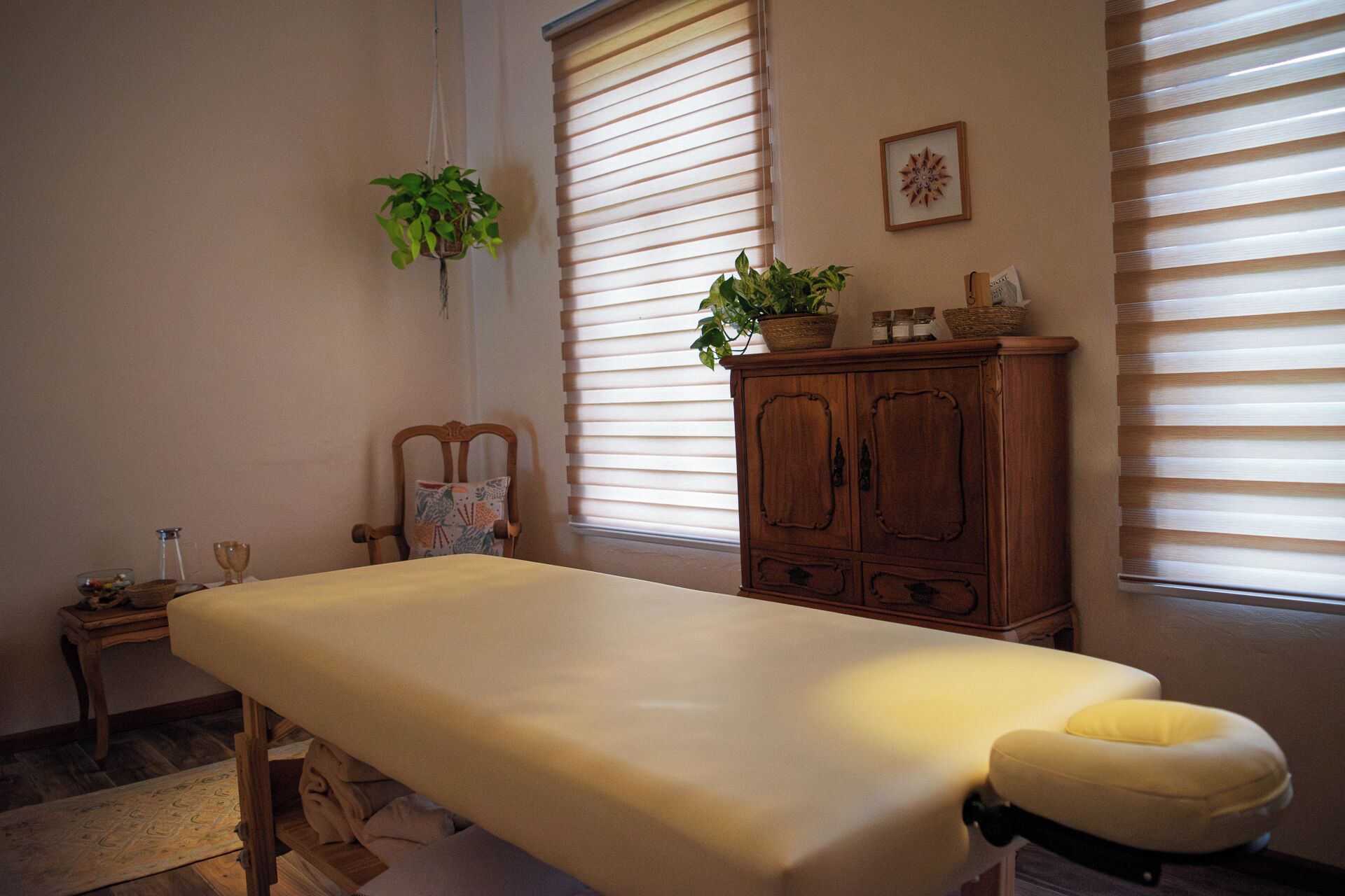 Quarto com mesa de massagem, um armário de madeira e duas janelas com persianas.