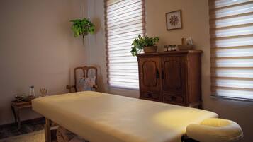 Quarto com mesa de massagem, um armário de madeira e duas janelas com persianas.