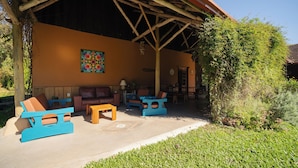 Un espacio de descanso al aire libre con techo, que incluye una estructura de madera, un sofá, dos sillones y una pequeña mesa.