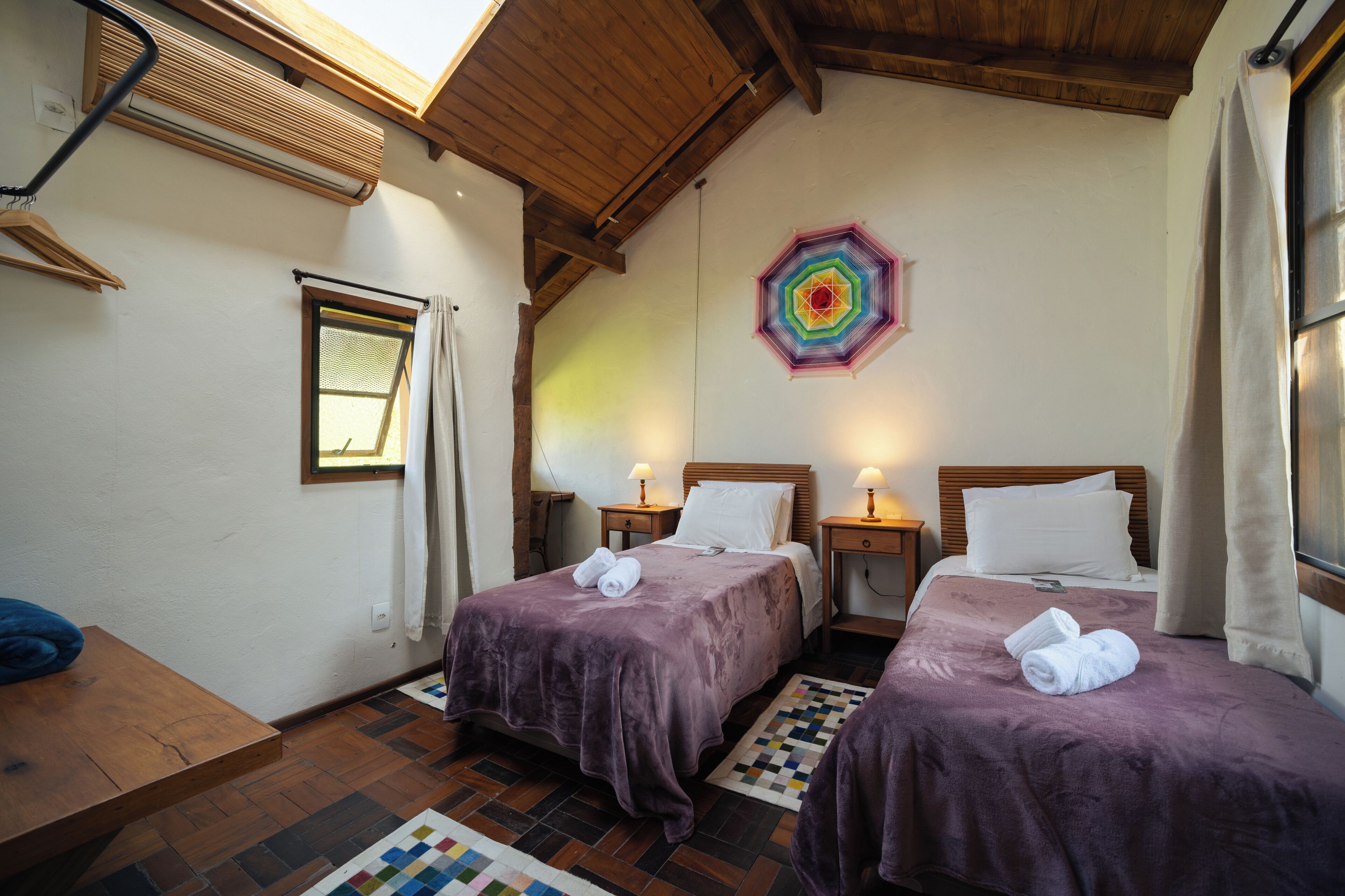 Una habitación con dos camas, techo de madera, decoración de pared colorida y una ventana con cortinas.