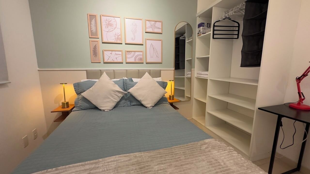 Een slaapkamer met een bed, nachtlampjes, een kledingkast en lijstjes met kunstwerken aan de muur.