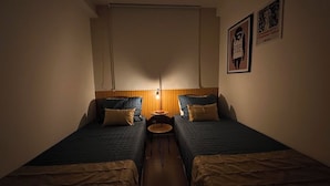 Een kleine kamer met twee eenpersoonsbedden, een tafeltje en een wandlamp.