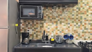 Een functionele keuken met een magnetron, koffiezetapparaat en een betegelde achterwand.