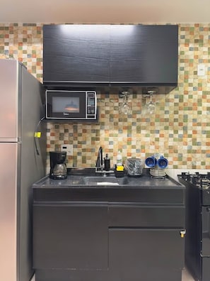Eine kompakte Küche mit Mikrowelle, Kaffeemaschine und einer gefliesten Spritzschutzwand.
