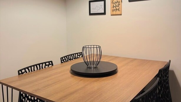 Een eethoek met een houten tafel, zwarte stoelen, een zwart hanglamp en lijstwerken aan de muur.