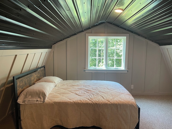 A bedroom with a bed, a window, and a sloped ceiling.