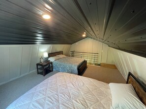 A small, sloped ceiling bedroom with two beds, a nightstand, and a lamp.