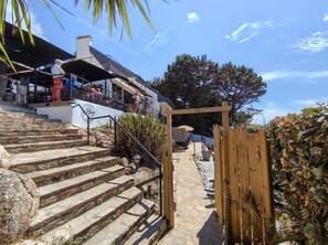 A stone staircase leading to a wooden gate, with a building and a tree in the background. - Cozy studio for 2 people — Les Villas de la Plage, Rospico (Névez) (Névez)
