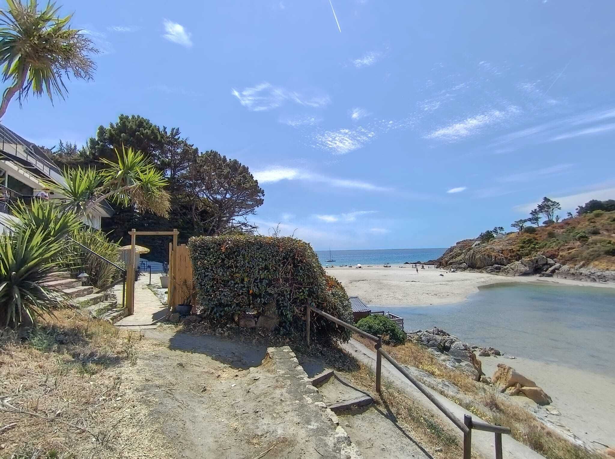 A coastal property with a paved pathway leading to a beach, a wooden structure, and a view of the sea.