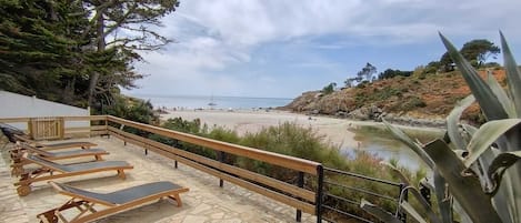 A stone deck with sun loungers overlooking a beach and a body of water.