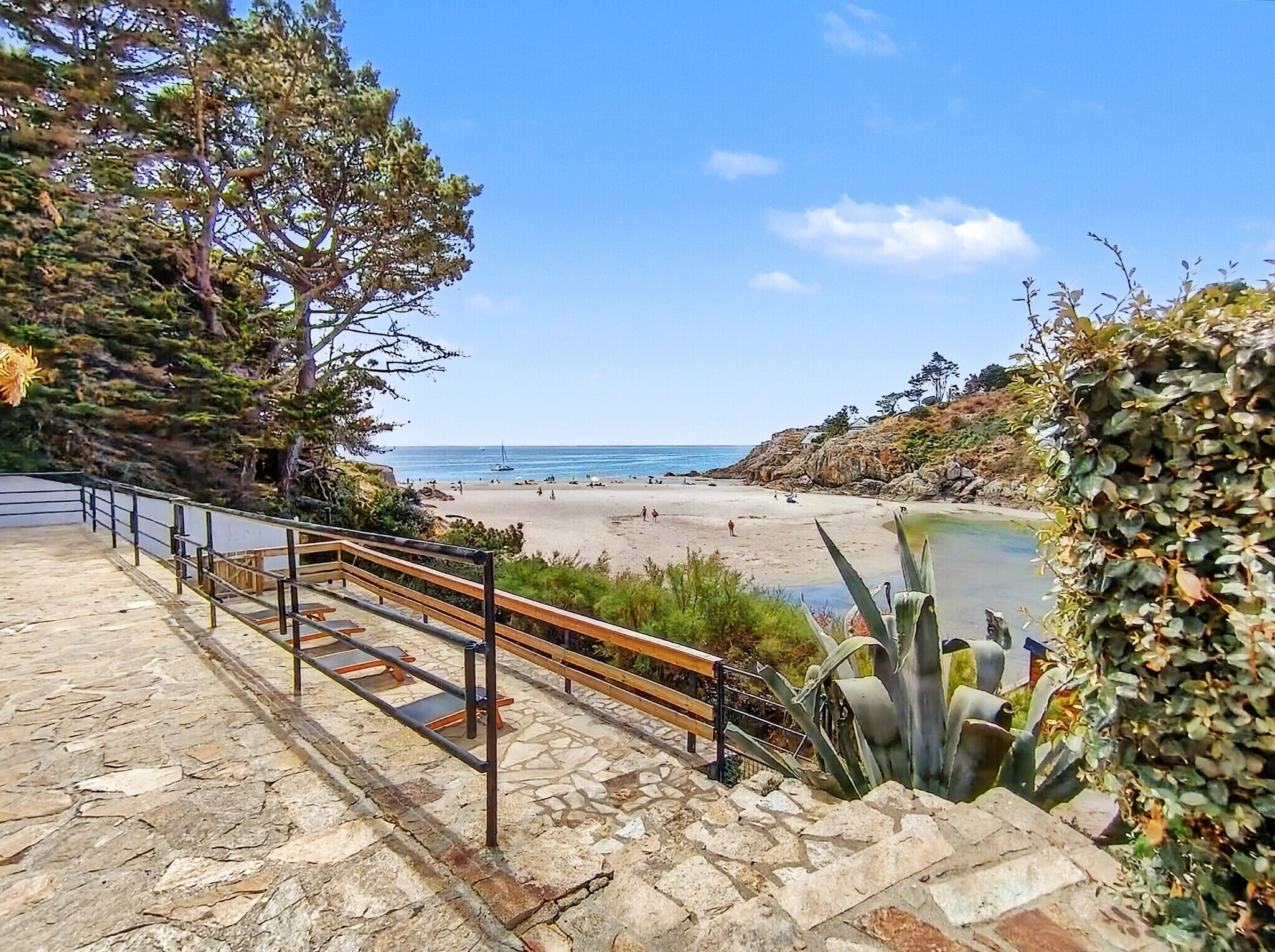 A stone staircase leading to a beach with a railing, a clear sky, and a calm sea.