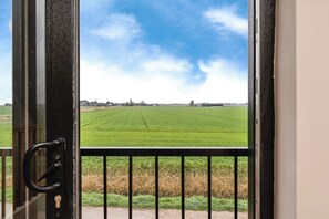 A view through a window with a metal railing, overlooking a green field and a clear sky. - Quaint 1-bedroom barn in Wimblington perfect for a peaceful stay (Wimblington)