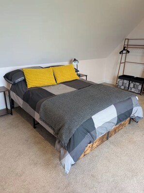 A bed with a grey and black quilt, two yellow pillows, a small bedside table with a lamp, and a black storage unit against the wall. - Quaint 1-bedroom barn in Wimblington perfect for a peaceful stay (Wimblington)