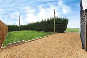 A gravel driveway leading to a wooden fence and a green lawn. - Quaint 1-bedroom barn in Wimblington perfect for a peaceful stay (Wimblington)