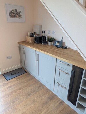 A kitchen with a wooden countertop, two black toasters, a coffee maker, a small potted plant, and a framed picture on the wall. - Quaint 1-bedroom barn in Wimblington perfect for a peaceful stay (Wimblington)
