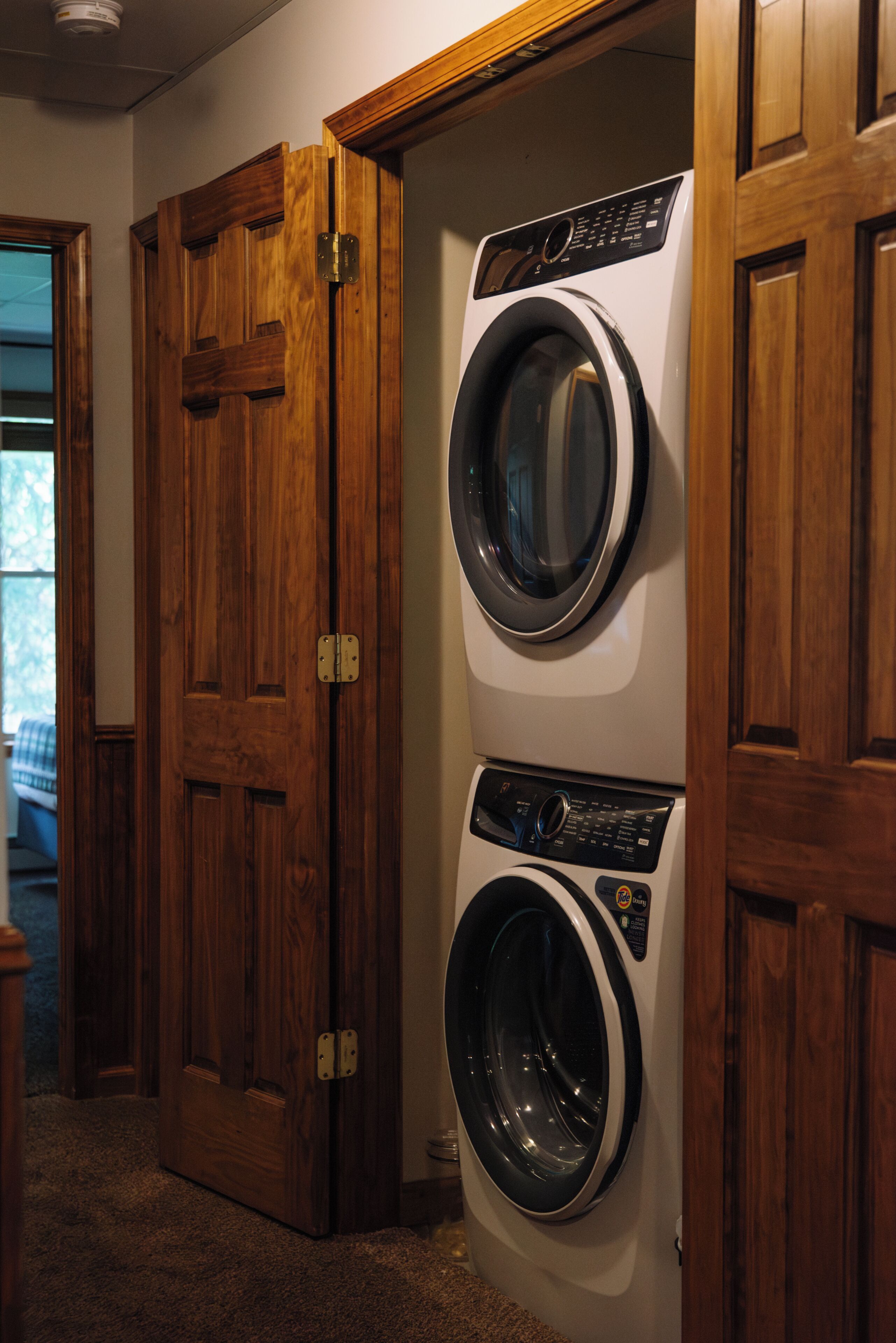 A laundry room with a front-loading washer and dryer, wooden doors, and a carpeted floor.