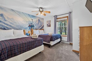 Ein Hotelzimmer mit zwei Betten, einem Deckenventilator, einem großen Fenster mit Vorhängen und einem Wandbild mit Bergmotiv.