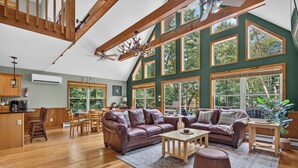 A spacious living area with high ceilings, large windows, and a modern kitchen. - Lake Harmony Chalet w/ Sauna, Hot tub,  Tensile Hammock, Game Room, Beach Passes (Lake Harmony)