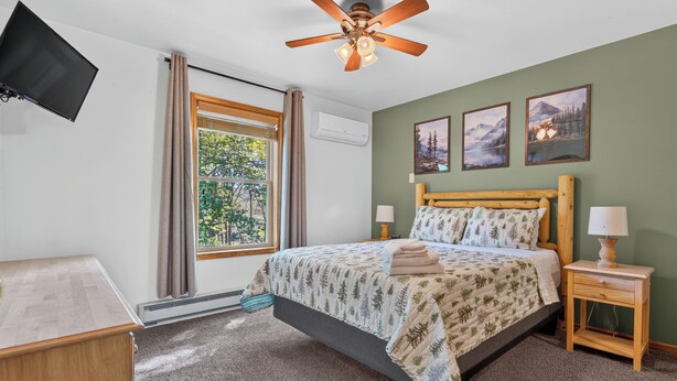 A bedroom with a bed, a nightstand, a TV mounted on the wall, and a ceiling fan. - Lake Harmony Chalet w/ Sauna, Hot tub,  Tensile Hammock, Game Room, Beach Passes (Lake Harmony)