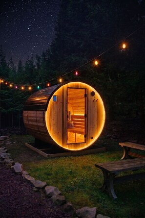 Eine baumartige Holzhütte mit warmem Innenlicht, umgeben von Lichterketten und einem Sternenhimmel.