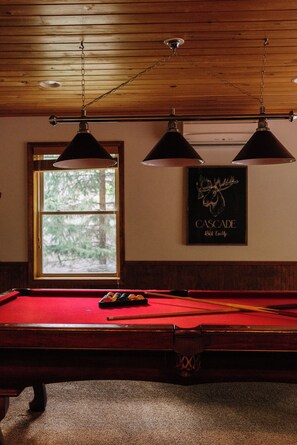 A pool table with a red felt surface, overhead lighting fixtures, and a framed picture on the wall. - Lake Harmony Chalet w/ Sauna, Hot tub,  Tensile Hammock, Game Room, Beach Passes (Lake Harmony)