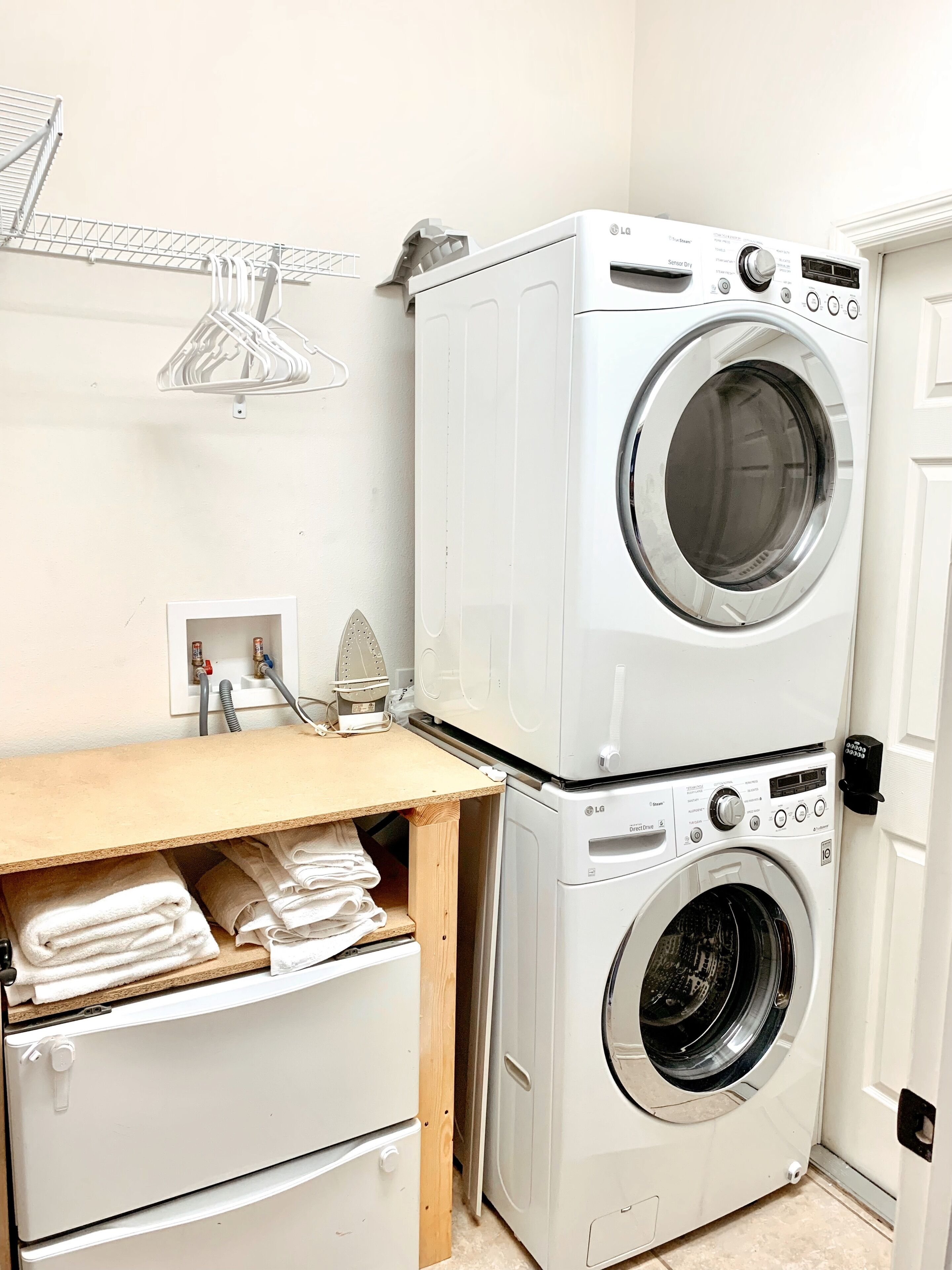 A laundry area with stacked washing machines, a drying rack, and a wooden table with towels.