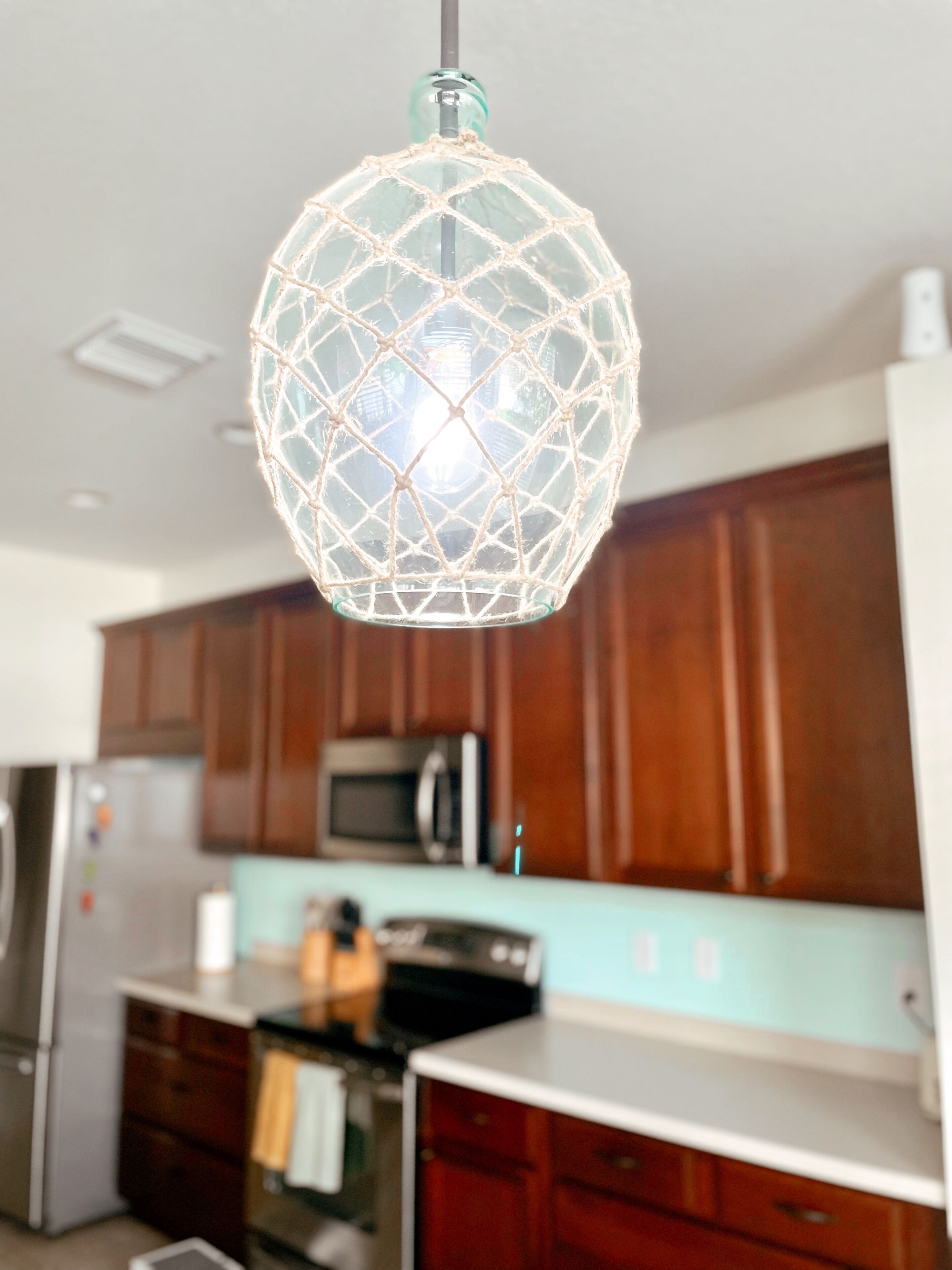 A kitchen with wooden cabinets, a microwave, and a hanging spherical light fixture.