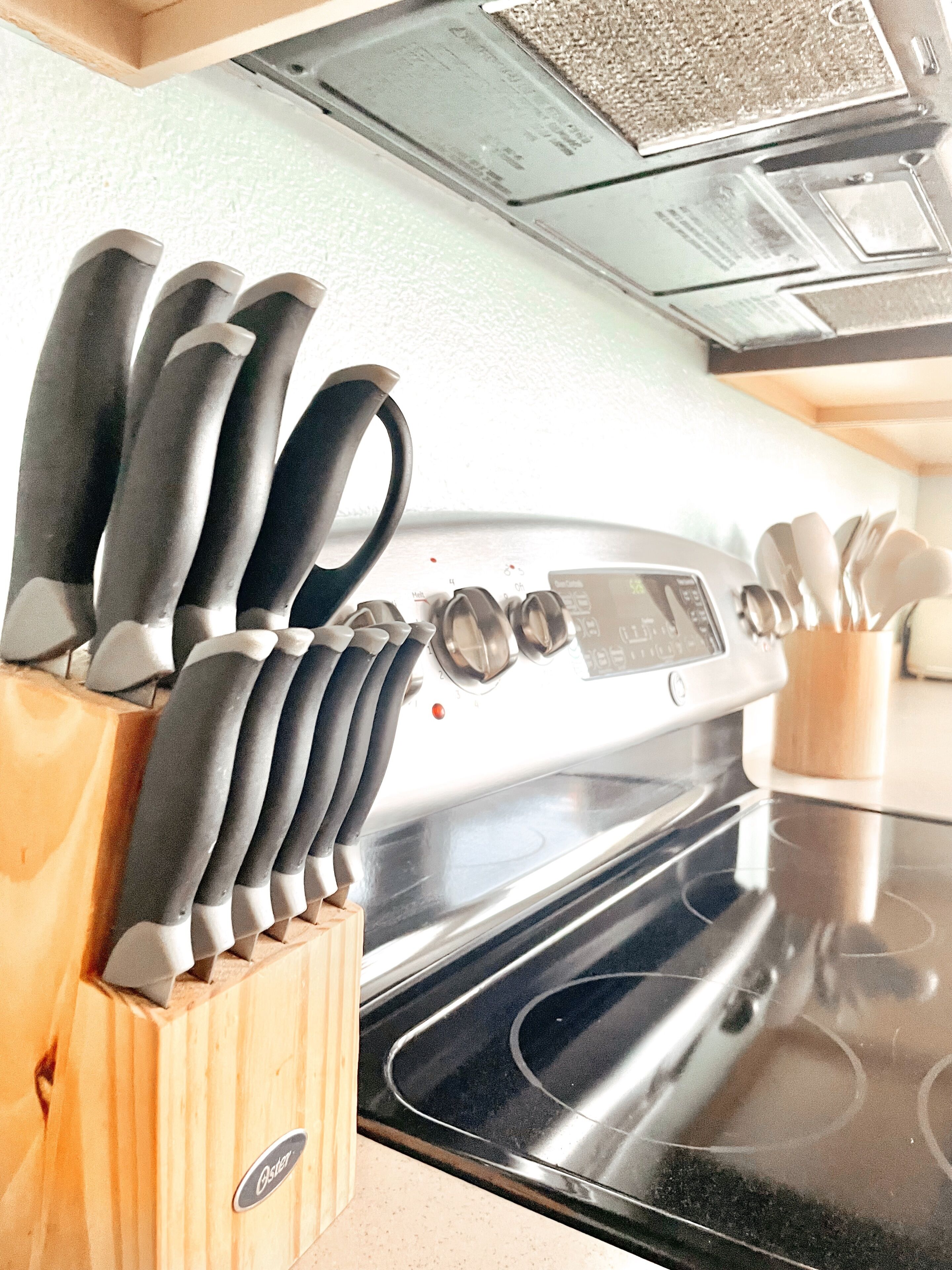 A kitchen with a stainless steel oven, a knife block with several knives, and a wooden cutting board.