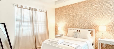 Une chambre à coucher comprenant un lit, un ventilateur de plafond, une table de chevet avec une lampe et un mur orné d’un motif en chevrons.