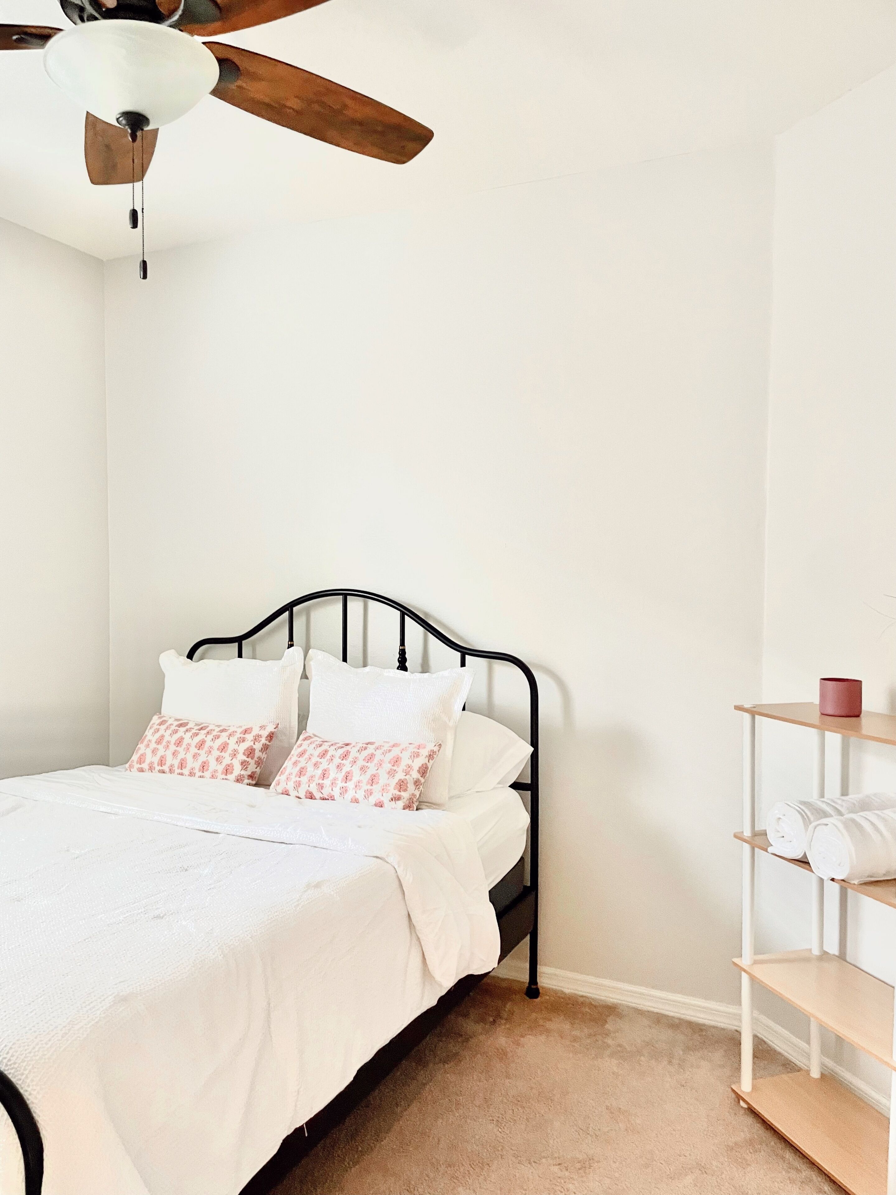 A bedroom with a bed, a ceiling fan, a bedside shelf with towels, and a white wall.