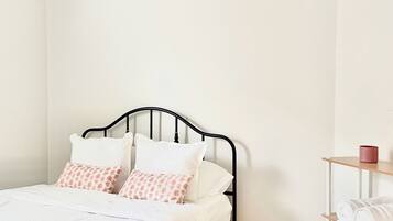 Une chambre avec un lit, un ventilateur de plafond, une étagère près du lit avec des serviettes et un mur blanc.