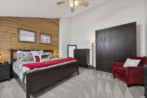 Ein Schlafzimmer mit Holzwand, einem Bett mit Blumenmuster auf der Bettwäsche, einem roten Sessel und einem Kleiderschrank.