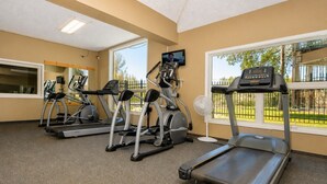 Une salle de sport équipée de tapis de course, de vélos elliptiques et d’un ventilateur.